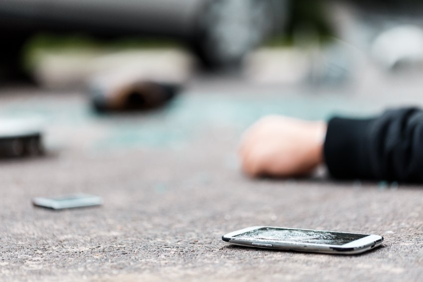 A smashed phone lying on the road next to the victim of a car crash