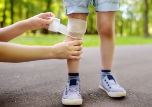 A woman bandages a child's knee with gauze in a park.