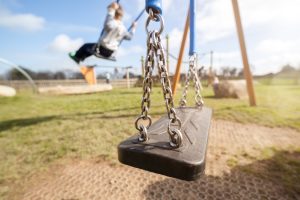 An empty swing on a playground with children playing around it.