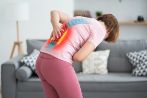 A woman hunched over holding her back in pain. The area is highlighted in red.