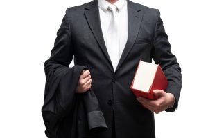 A multiple injury lawyer in a suit carrying his blazer jacket in one hand and a red law book in the other.