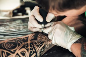 A male tattoo artist tattooing someone's arm.