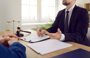 A solicitor sits and holds out their left arm as they explain pavement accident claims to their client.