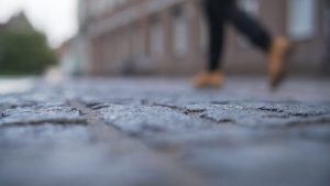 A person walking on a pavement. In the foreground, the pavement appears cracked and broken.