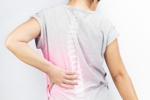 A person holds her back with their spinal column highlighted. 